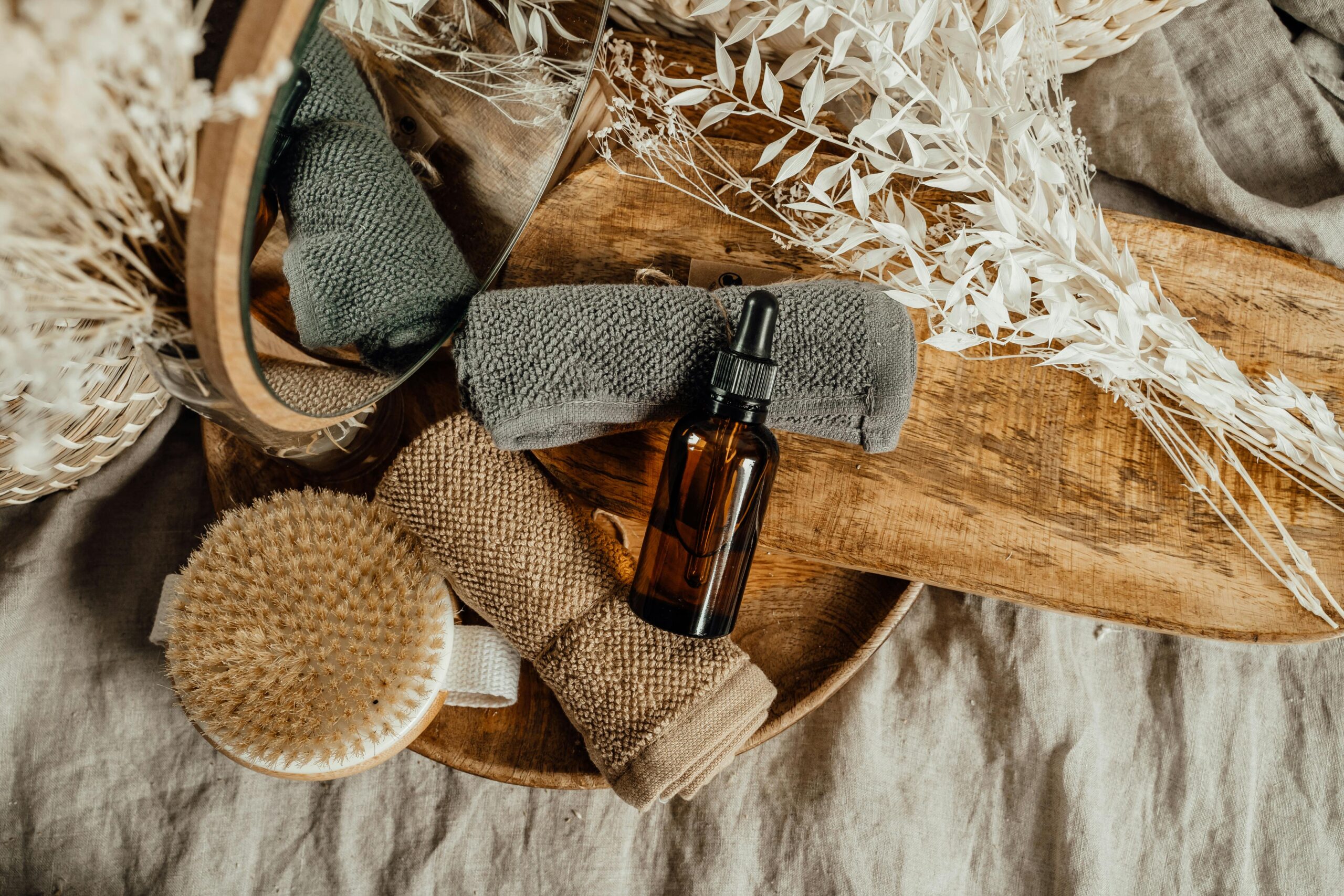 A serene spa setting with essential oil, towels, and dried flowers on a wooden tray.